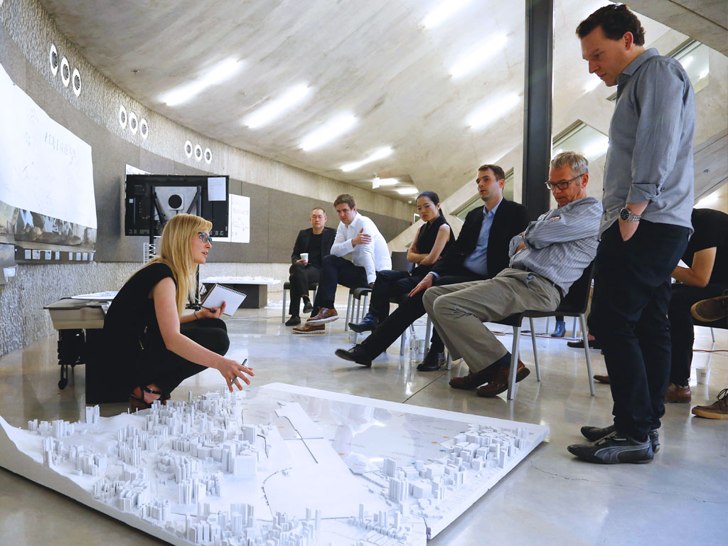 A woman kneeling in front of a model, talking to a small audience
